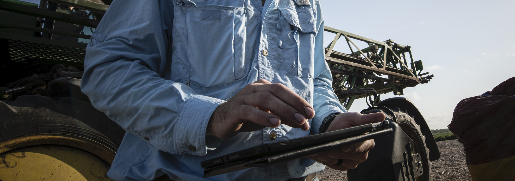 close shot of farmer using tablet with large vehicle in the background